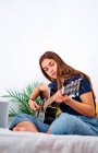 Studentessa concentrata a guardare video tutorial sul laptop mentre impara a suonare la chitarra acustica durante il tempo libero a casa — Foto stock
