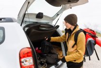 Side view of content female adventurer standing with traveling backpack near car trunk in mountains — Stock Photo