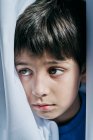 Petit garçon malheureux regardant derrière les rideaux tout en souffrant de violence domestique et se cachant des parents — Photo de stock