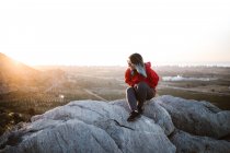 Живописный вид молодого туриста, сидящего на вершине горы и смотрящего в солнечный день — стоковое фото