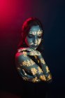 Модна молода жіноча модель зі світлою проекцією у формі східних ієрогліфів, що дивиться вниз в темну студію з червоним освітленням — стокове фото