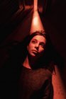 De cima de fêmea jovem silenciosa deitada no chão em quarto escuro com luz brilhando de porta aberta olhando para longe — Fotografia de Stock