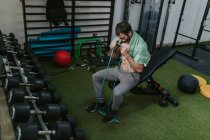 Uomo senza maglietta seduto su una panchina che allunga elastico con le braccia durante l'allenamento funzionale in palestra — Foto stock