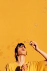 Mujer moderna con burbujas de jabón perforantes en un día soleado contra la pared amarilla - foto de stock