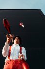 D'en bas jeune artiste de cirque masculin qualifié jonglant avec le club sur le bâtiment moderne — Photo de stock