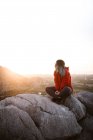 Pittoresca veduta del giovane turista seduto sulla cima della montagna e distogliendo lo sguardo nella giornata di sole — Foto stock