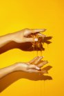 Culture femelle méconnaissable montrant la main avec manucure et des liquides de miel aromatiques sur fond jaune avec de l'ombre — Photo de stock