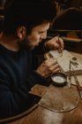Manos de Goldsmith cortando metal con sierra mientras hace joyas en taller - foto de stock