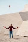 Volle Länge des männlichen Kunststücks mit Jonglierkeulen beim Stehen gegen zeitgenössische Steinbauten mit ungewöhnlicher geometrischer Architektur — Stockfoto