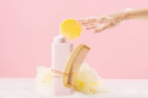Front view of still life of a bottle of bath gel with a comb and a sponge ready to be used while an anonymous woman's hand touches the sponge — Stock Photo