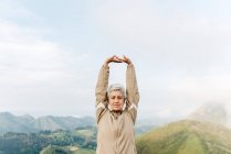 Soft focus of senior female traveler stretching arms and warming up during trip in hilly terrain — Stock Photo