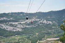 Anonyme Mutige in Sicherheitsausrüstung fahren im Sommer Seilrutsche über die Berge — Stockfoto
