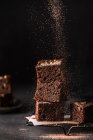 Composición de una pequeña pila de sabrosos cortes de brownie dulce con polvo sobre fondo negro - foto de stock