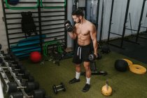 Muscular young male trainer with naked torso lifting heavy dumbbells while training in gym — Stock Photo