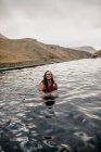 Joven hipster tatuado alegre en traje de baño en el agua entre las montañas - foto de stock