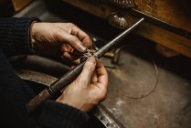 Goldsmith masculino barbudo usando pinças ao fazer minúsculo detalhe de metal na bancada na oficina — Fotografia de Stock