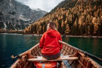 Back view of unrecognizable blonde woman on wooden boat with paddles floating on turquoise water of calm lake on background of majestic landscape of highlands in Dolomites in Italy alps looking away — Stock Photo