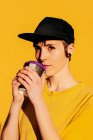 Jovem fêmea informal na moda tampão bebendo takeaway bebida quente contra fundo amarelo — Fotografia de Stock
