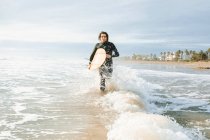 Surfer man dressed in wetsuit running with surfboard on the beach during sunrise — Stock Photo
