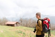 Vista laterale del viaggiatore femminile pensieroso con zaino che cammina in montagna guardando la fotocamera — Foto stock