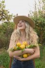 Donna positiva con bocca aperta in piedi con agrumi in mano nel frutteto durante la stagione della raccolta — Foto stock