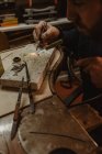 Bearded male goldsmith using tongs while making tiny metal detail on workbench in workshop — Stock Photo