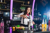 Femme barman en tenue élégante ajoutant des glaçons dans un verre tout en préparant un cocktail debout au comptoir dans un bar moderne — Photo de stock