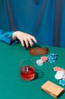 Обрізати невпізнавану жінку з картками і фішками, граючи в покер, сидячи за зеленим столом — стокове фото