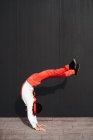 Vista lateral de un artista de circo masculino ágil irreconocible haciendo truco de salto mortal contra la pared negra - foto de stock