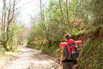 Vue arrière de randonneuse anonyme marchant le long de la route dans les bois pendant l'aventure en été — Photo de stock