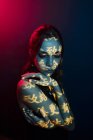 Модная молодая женская модель со светлой проекцией в виде восточных иероглифов, смотрящая вниз в темную студию с красным освещением — стоковое фото