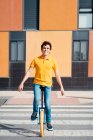 Talented man in casual wear sitting on unicycle crossing road on zebra on modern urban street with colorful building — Stock Photo