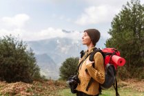 Seitenansicht einer unbeschwerten Backpackerin, die im Hochland steht und die Natur auf Reisen im Sommer genießt — Stockfoto