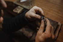 Unrecognizable goldsmith holding gem and metal ornament over table while making ring in workshop — Stock Photo