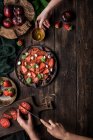 Anonymous people preparing a healthy tomato and strawberry salad on a wooden rustic table — Stock Photo