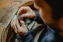Gioielliere anonimo che tiene anello incompiuto in mani sporche e controlla la qualità in officina — Foto stock