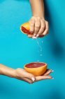 Анонімна жінка з манікюром, що стискає половину свіжого стиглого соковитого грейпфрута на синьому фоні — стокове фото