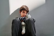 Perturbado solitário pré-adolescente menino vítima de violência doméstica sentado no chão e abraçando brinquedo — Fotografia de Stock