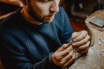 Joyero sosteniendo anillo inacabado en manos sucias y comprobando la calidad en el taller - foto de stock