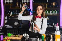 Garçonete focado feminino em roupa elegante adicionando líquido de garrafa em jigger enquanto prepara coquetel em pé no balcão no bar moderno — Fotografia de Stock