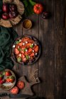 Unbekannte bereiten auf einem rustikalen Holztisch einen gesunden Tomaten- und Erdbeersalat zu — Stockfoto