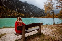 Back view of unrecognizable woman sitting on bench looking at lake in Dolomites in Italy — Stock Photo