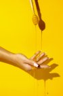 Coltura femminile irriconoscibile mostrando mano con manicure e fluidi aromatici miele su sfondo giallo con ombra — Foto stock