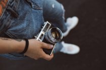 From above crop hands of people in casual wear and white sneakers holding vintage camera on blurred background — Stock Photo