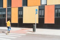 Back view of unrecognizable talented man in casual wear sitting on unicycle crossing road on zebra on modern urban street with colorful building — Stock Photo