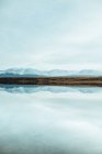 Pittoresca vista della superficie dell'acqua vicino a incredibili colline rocciose nella neve e nel cielo blu — Foto stock