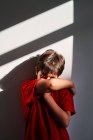 Upset unrecognizable boy covering face with hands and crying while standing near wall at home — Stock Photo
