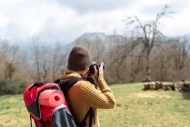 Vista posterior de una mochilera anónima tomando fotos del paisaje montañoso durante el viaje - foto de stock