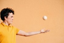 Jovem talentoso macho realizando truque com bolas de malabarismo enquanto em pé no pavimento perto de parede laranja brilhante — Fotografia de Stock