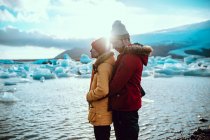 Seitenansicht von jungen Männern und Frauen in Winterbekleidung mit professionellen Kameras, die am Ufer in der Nähe von Wasser mit Eis stehen — Stockfoto